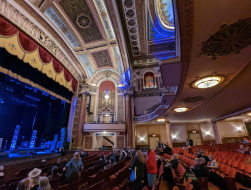 Interior of a grand theater with ornate architecture, empty seats, and a stage set for a performance.