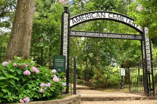Entrance to American Cemetery, the oldest cemetery in the Louisiana Purchase, featuring a decorative arch and blooming flowers.
