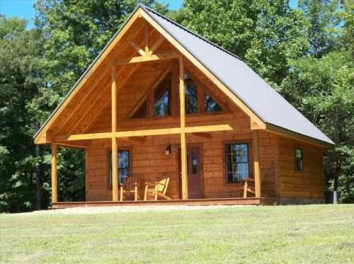 A charming wooden cabin with a sloped roof, surrounded by trees and featuring a porch with two chairs.