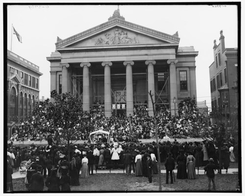 A large crowd gathers in front of a grand building with columns, likely for a public event or celebration.