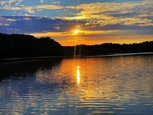 A serene sunset over a calm lake, with vibrant orange and blue hues reflecting on the water's surface.