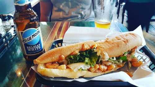 A shrimp sandwich with lettuce on a tray, accompanied by a bottle of Blue Moon beer.