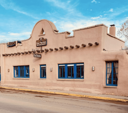 A southwestern-style restaurant with a stucco exterior, blue windows, and a curved roof against a cloudy sky.