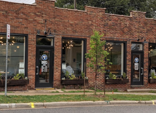 A brick building with large windows, featuring a sign for "Roger's" and planters along the sidewalk.