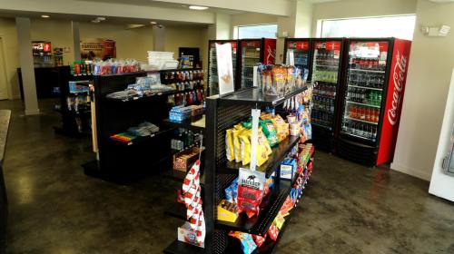 A convenience store interior with shelves of snacks, drinks, and various merchandise, featuring Coca-Cola vending machines.