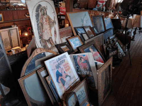 A collection of vintage framed artwork and mirrors displayed in a rustic interior setting.