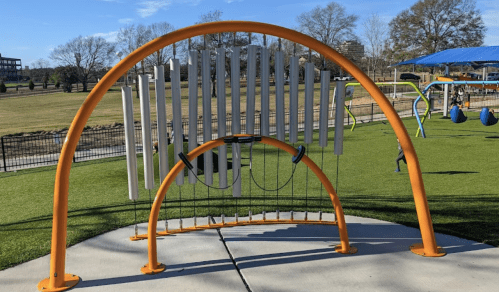 Colorful outdoor musical instrument with vertical bars, set in a playground with green grass and blue sky.