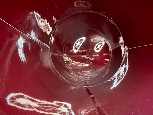 A close-up view inside a shiny, red tunnel with reflections creating a wavy pattern on the surface.