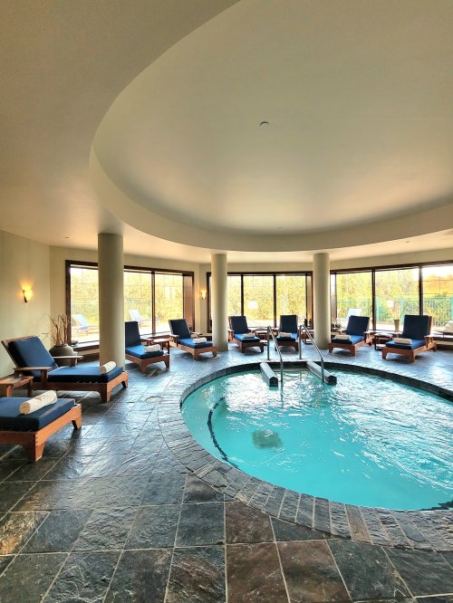 A serene spa area featuring a circular hot tub and lounge chairs, surrounded by large windows and natural light.