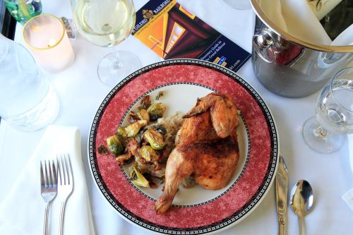 A plate with roasted chicken, Brussels sprouts, and rice, set on a table with glasses and a candle.