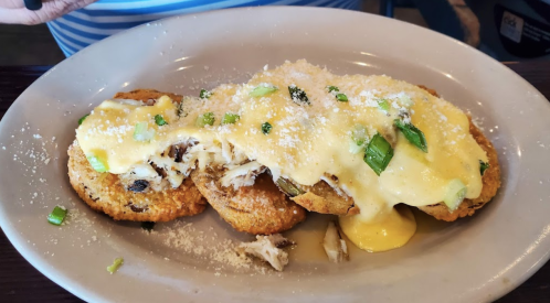 Three fried green tomatoes topped with crab meat, creamy sauce, and green onions, served on a white plate.