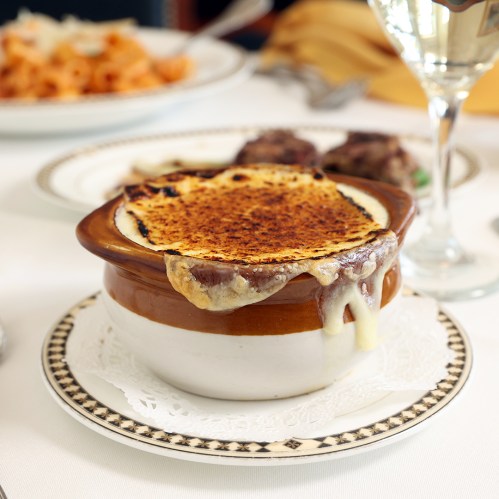 A bowl of French onion soup topped with melted cheese, served on a decorative plate.