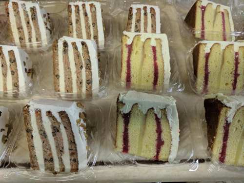 A display of layered cakes with white frosting and raspberry filling, arranged in clear plastic containers.