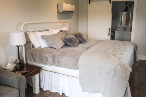Cozy bedroom featuring a large bed with decorative pillows, a bedside lamp, and a view of a bathroom area.
