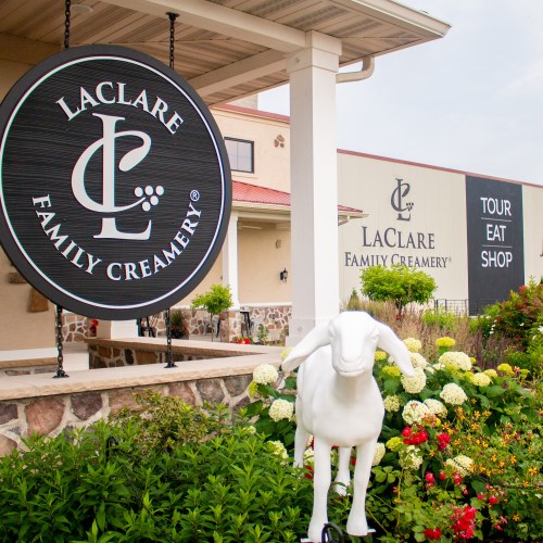 Sign for LaClare Family Creamery with a white goat statue and colorful flowers in the foreground.