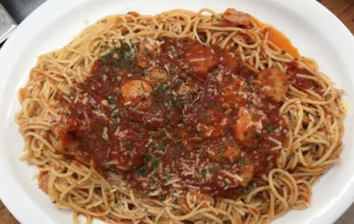 A plate of spaghetti topped with shrimp and marinara sauce, garnished with herbs and grated cheese.