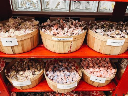 Baskets of assorted candies labeled Honey, Neapolitan, Candy Bar, and more, displayed on a red shelf.