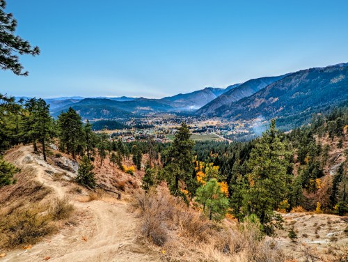 A scenic view of a valley surrounded by mountains, with a winding path and trees in autumn colors under a clear blue sky.