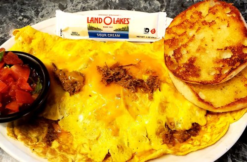 A large omelette filled with cheese and meat, served with sour cream, diced tomatoes, and two toasted bread slices.