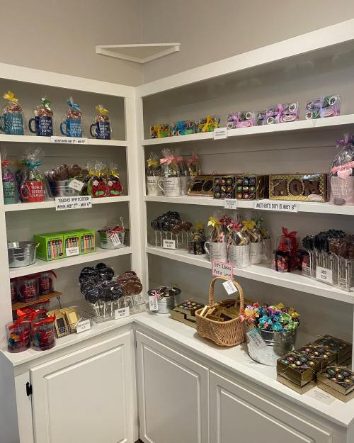 A display of colorful candies, chocolates, and gifts arranged on shelves in a shop, with a basket in the foreground.