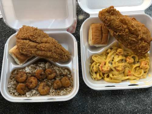 Two takeout containers: one with fried chicken, rice, and shrimp; the other with fettuccine and shrimp, plus a roll.