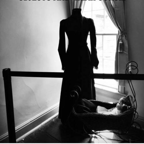 A vintage dress stands beside a cradle with a doll, illuminated by soft light from a nearby window.