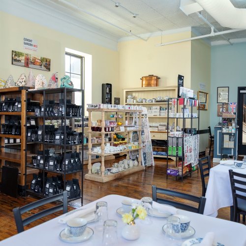 A cozy shop interior with wooden shelves displaying tea, ceramics, and kitchenware, set with tables for dining.
