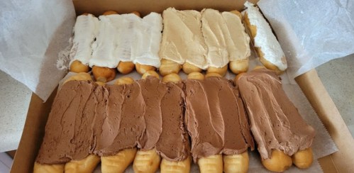 A box of cream-filled pastries topped with white, beige, and chocolate frosting.