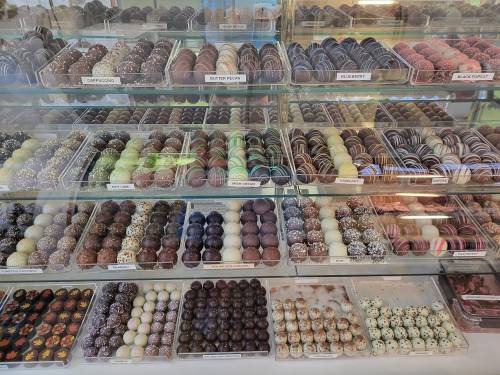 A display case filled with various types of colorful chocolates and truffles, neatly arranged in rows.