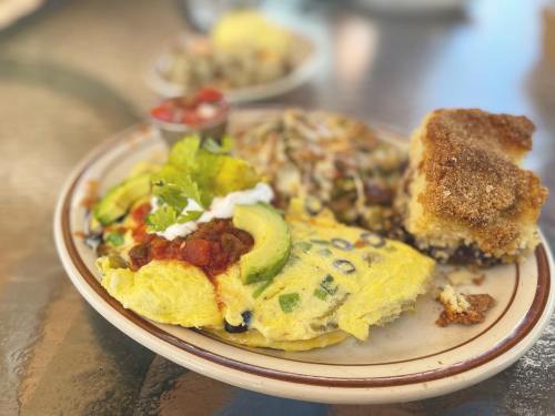 A plate of colorful omelette with avocado, salsa, and sour cream, served with hash browns and a piece of cornbread.