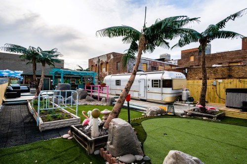 A colorful outdoor space featuring palm trees, a vintage trailer, and playful decor like flamingos and garden rocks.