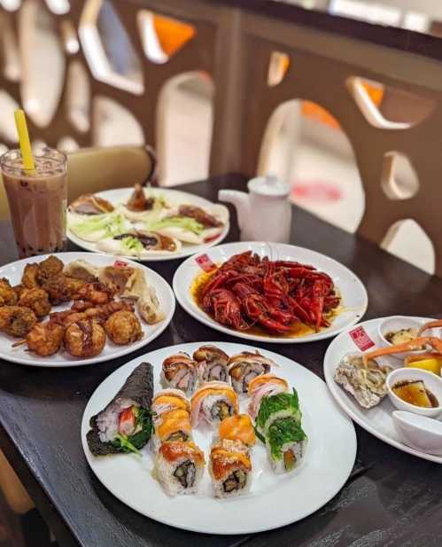 A table spread with sushi, crawfish, fried chicken, and drinks, showcasing a variety of colorful dishes.