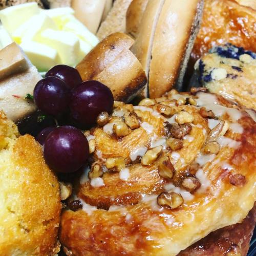 A close-up of assorted baked goods, including pastries, bread, and grapes, with a focus on a nut-topped pastry.