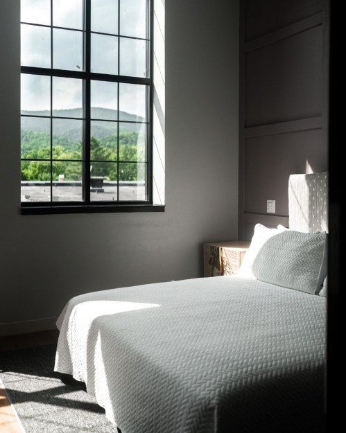 Bright bedroom with a white bedspread, large window showcasing a green landscape outside.