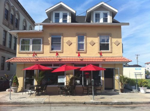 A two-story building with a yellow exterior, featuring red umbrellas over outdoor seating and an "Open" sign.