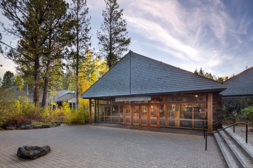 A modern building with large windows, surrounded by trees and colorful foliage under a clear sky.