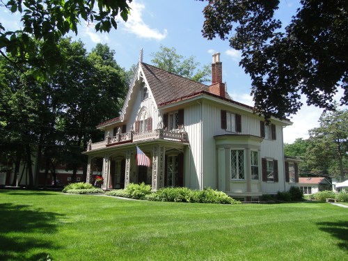 A charming Victorian-style house with a gabled roof, surrounded by lush green grass and trees on a sunny day.