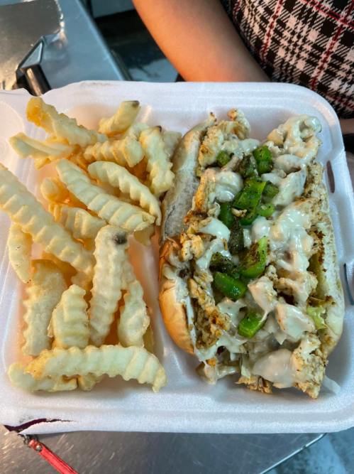 A plate with a chicken sandwich topped with green peppers and mayonnaise, served with crinkle-cut fries.