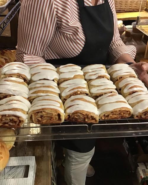 A person holds a tray of freshly baked cinnamon rolls drizzled with white icing.