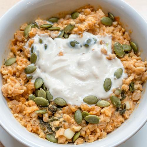 A bowl of oatmeal topped with yogurt and pumpkin seeds, featuring a creamy texture and a warm, inviting color.