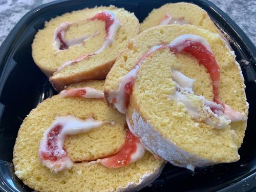 Sliced yellow cake roll filled with strawberry jam and cream, arranged in a black container.