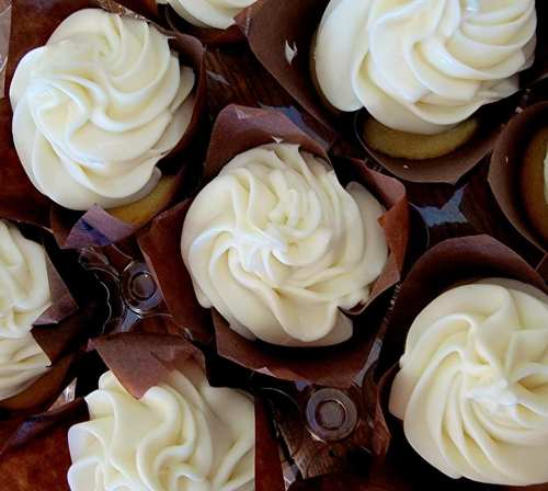 A close-up of beautifully frosted cupcakes with swirls of white icing in brown paper wrappers.