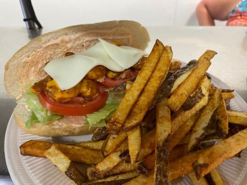 A sandwich with lettuce, tomato, and cheese, served with a side of crispy French fries on a white plate.