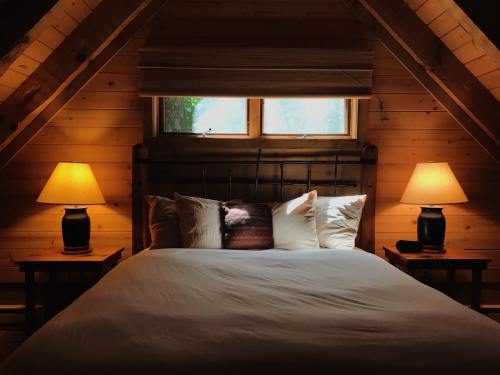 Cozy attic bedroom with a large bed, two lamps, and wooden walls, illuminated by natural light from the windows.