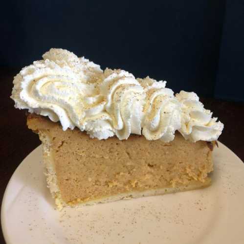 A slice of creamy pumpkin pie topped with whipped cream and a sprinkle of cinnamon on a white plate.