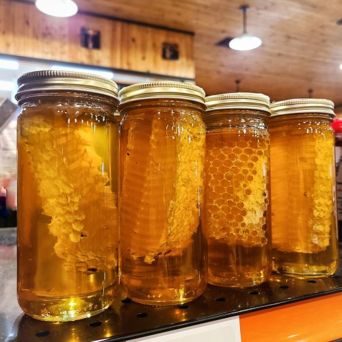 Four jars of honey filled with honeycomb, displayed on a counter in a rustic setting.