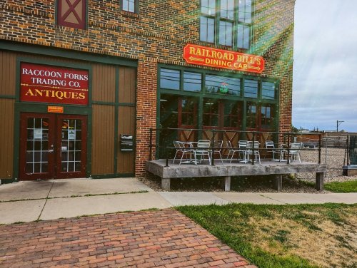 Exterior of a brick building featuring "Railroad Bill's Dining Car" and "Raccoon Forks Trading Co. Antiques" signs.