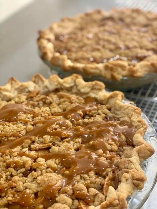 Two freshly baked pies with crumbly topping and caramel drizzle, cooling on a wire rack.