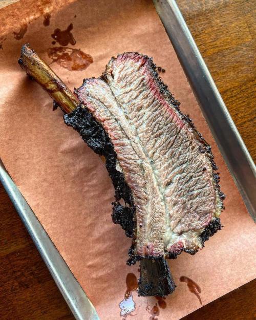 A large, smoked beef rib resting on brown butcher paper, showcasing a smoky crust and juicy interior.