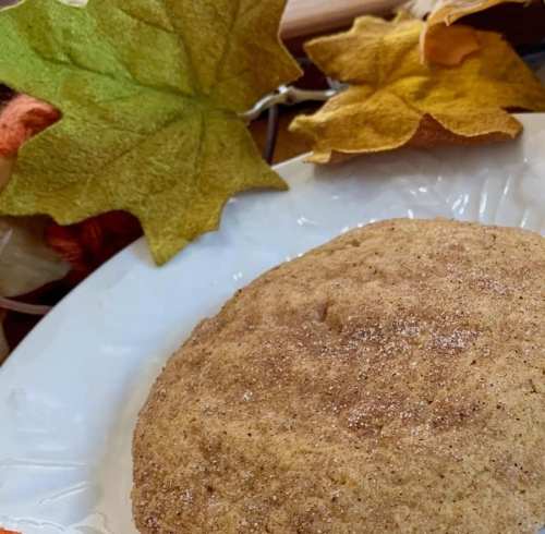 A round, brown baked good on a white plate, surrounded by colorful autumn leaves.